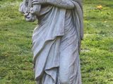 une statue représentant une femme tenant un chien dans un champ herbeux
