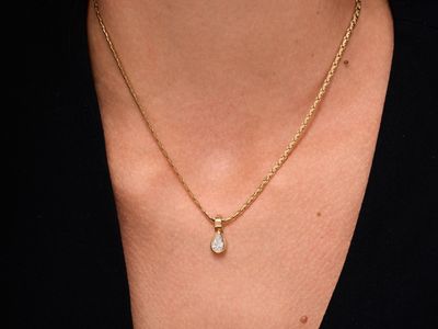 a close up of a woman wearing a gold necklace with a tear