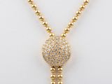a gold necklace with a ball and a tassel on a mannequin