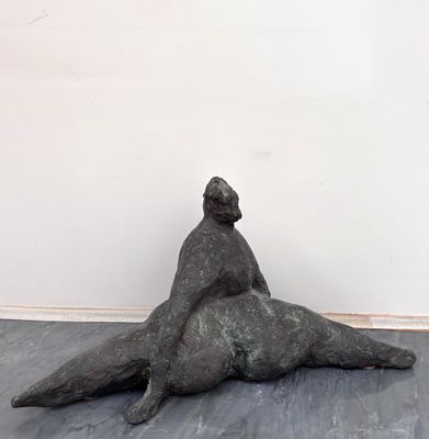 statue représentant une femme assise sur le dos d'un homme, posée sur un plancher en bois