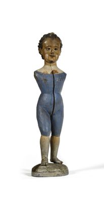 une petite statue en bois représentant un garçon debout sur un socle