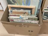 une boîte en carton remplie de tableaux et de photos, posée par terre