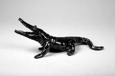 figurine d'alligator noir assis sur une surface blanche, la gueule ouverte