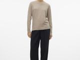 a woman in a beige sweater and black pants stands in front of a white background