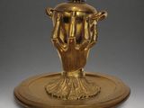 an image of a gold plate with a hand holding a teapot on it