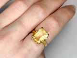 a woman ' s hand holding a ring with a yellow stone on it
