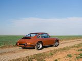an orange car driving down a dirt road next to a green field