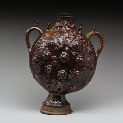 un vieux vase marron muni d'une anse et de poignées sur un fond gris