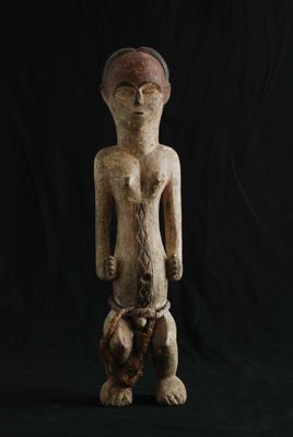 une statue en bois représentant un homme debout sur un fond noir