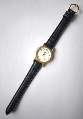 gros plan d'une montre sur une surface blanche avec un bracelet noir
