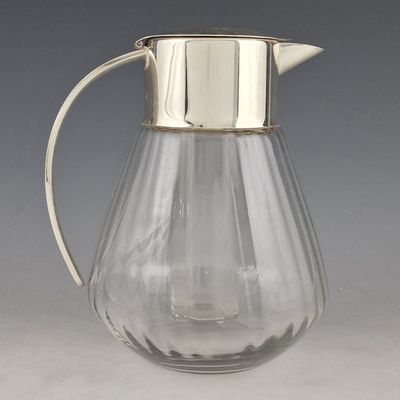 un pichet en verre avec un couvercle en argent posé sur une table