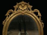 a gold framed mirror with a man ' s reflection in it