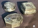three silver boxes sitting on a table with a brown cloth