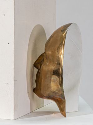 sculpture représentant une tête dorée posée sur un socle blanc, avec un fond blanc