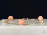 a gold chain bracelet with peach beads and pearls