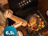 une femme en train de préparer un repas dans une friteuse à air chaud posée sur une table en bois