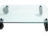 a glass coffee table with wheels and a vase on it