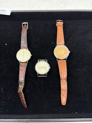Trois montres différentes sont exposées dans une vitrine posée sur une table.