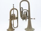 two antique brass trumpets sitting next to each other on a white surface