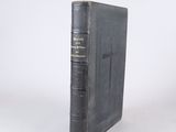 an old book with a black cover sitting on top of a white surface
