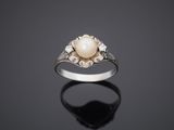 a white pearl and diamond ring on a black surface
