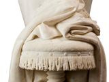 a statue of a woman sitting on a stool with a blanket on it