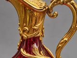a red glass pitcher with gold decoration on it