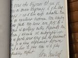 un livre ouvert, sur lequel est inscrit un poème manuscrit, posé sur une table