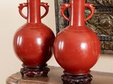 deux vases rouges posés sur une table en bois, à côté d'un miroir