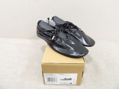 Des chaussures en cuir noir ornées de pompons sont posées sur une boîte