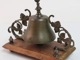 une petite cloche posée sur un socle en bois, sur fond blanc