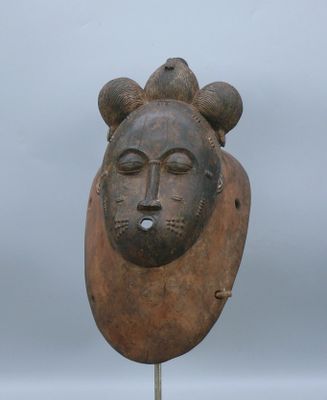 sculpture représentant un visage posée sur un socle en bois, avec un ciel gris en arrière-plan