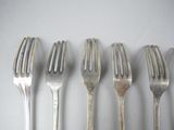 six forks are lined up in a row on a white surface