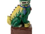 statue of a green and yellow dog sitting on top of a wooden block