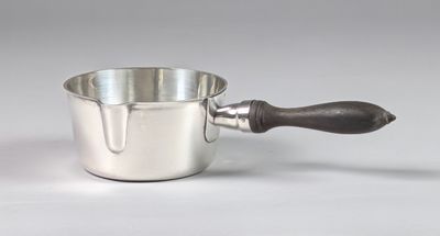 une saucière en argent avec un manche en bois, posée sur un plan de travail blanc