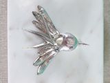 a silver bird with a pearl in its beak on a white plate