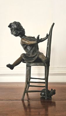 une statue en bronze représentant un enfant assis sur une chaise