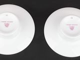 two white plates with red writing on them sitting on a black surface