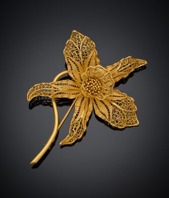 une broche en forme de fleur plaquée or, ornée de feuilles, sur fond noir