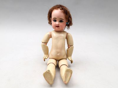 une petite poupée assise par terre sur un fond blanc