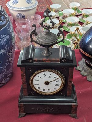 a small clock sitting on a table next to a vase