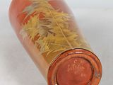 a red vase with yellow leaves on it sitting on a white surface
