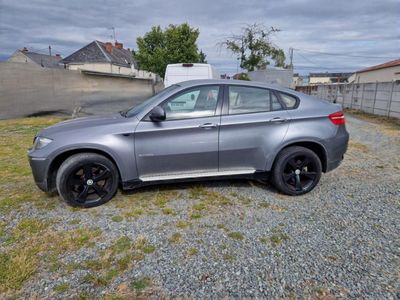 the bmw x6 is parked on the gravel in the yard