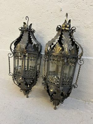 une paire de lanternes anciennes en métal accrochées à un mur blanc, à côté d'un autre mur blanc