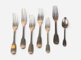 six forks and a spoon are arranged in a row on a white surface