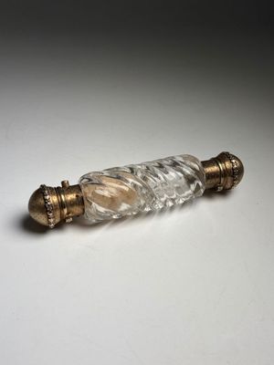 a small glass bottle with a gold handle on a white surface