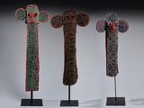 trois sculptures en bois de couleurs différentes, posées sur des socles, devant un fond noir