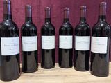 six bottles of red wine are lined up on a wooden table
