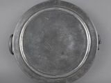 an old silver plate with a handle on a gray surface