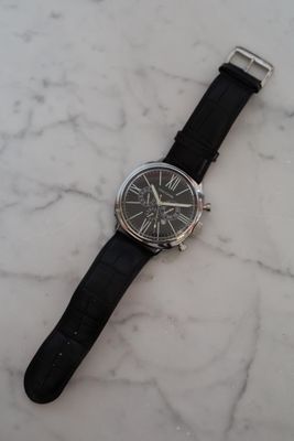 the watch is sitting on a marble surface with a black strap